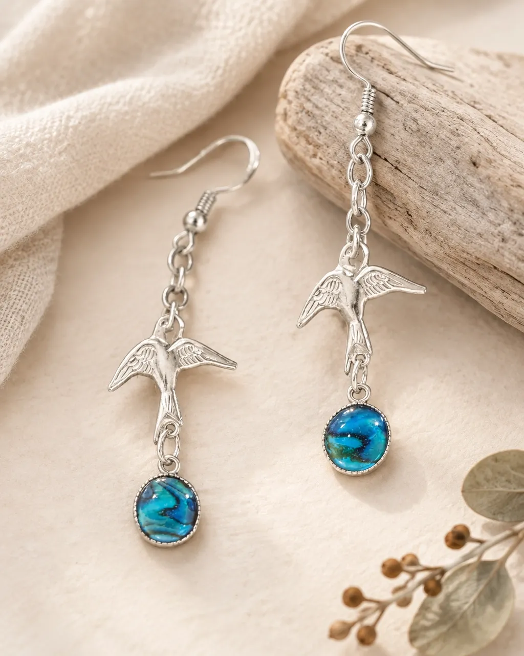 Handmade silver swallow earrings with blue abalone stones on linen